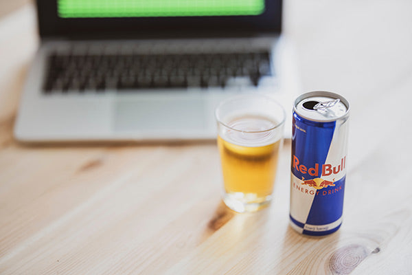 muscle cramps 101 causes and natural remedies glass and can of red bull energy drink sitting on a wooden able next to a laptop