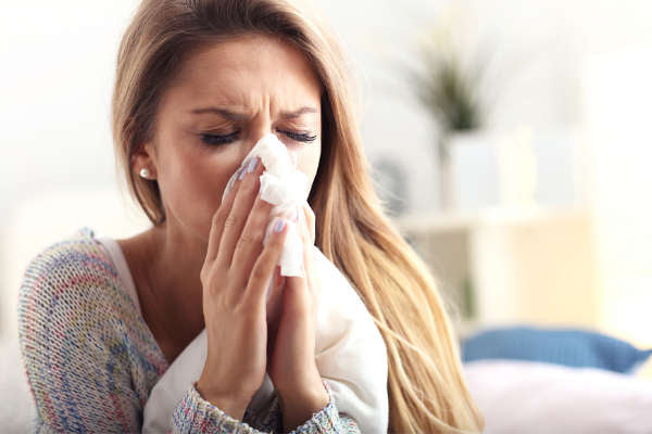 Blonde woman sneezing into tissue