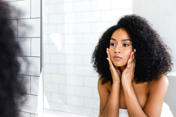 Woman moisturizing skin while looking in mirror 