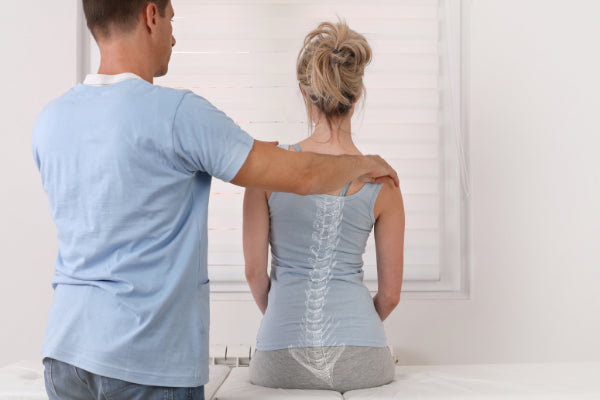 scoliosis back pain how to relieve it woman getting her back checked out at doctors office diagnosis white room