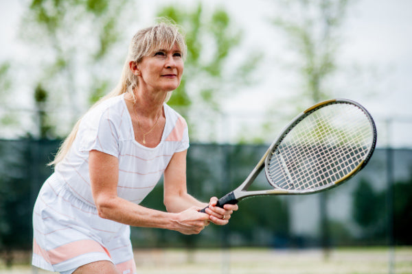 tendonitis vs tendinosis what is the difference middle aged woman wearing white striped jumper in a tennis stance with a racket in her hand