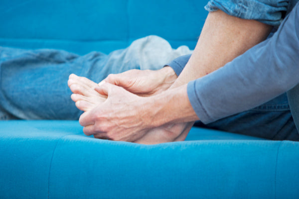 top 10 causes of joint pain person sitting on blue couch wearing blue holding toes in pain from gout