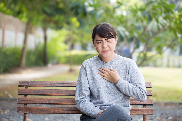 turmeric health benefits turmeric essential oil benefits woman sitting on park bench holding chest because of heart burn