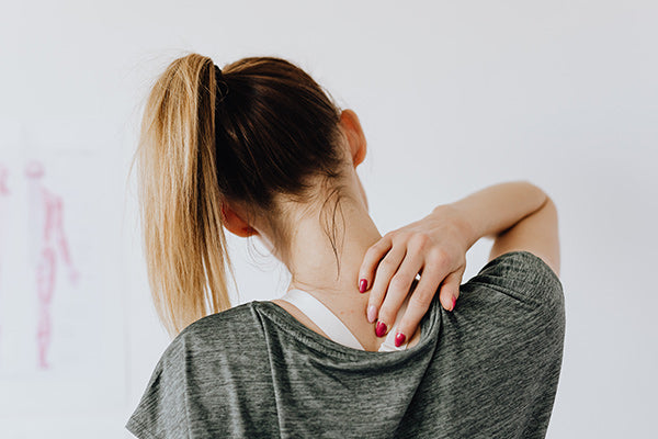 using dmso for muscle pain relief woman person touching the back of her neck from muscle pain gray shirt in the doctors office blurred background