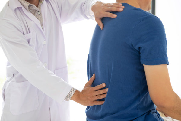 what is ankylosing spondylitis ankylosing spondylitis symptoms causes natural treatments doctor feeling the lower back of male patient in blue t shirt due to pain in office