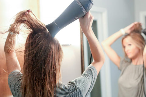 Woman blow drying her hair in the mirror