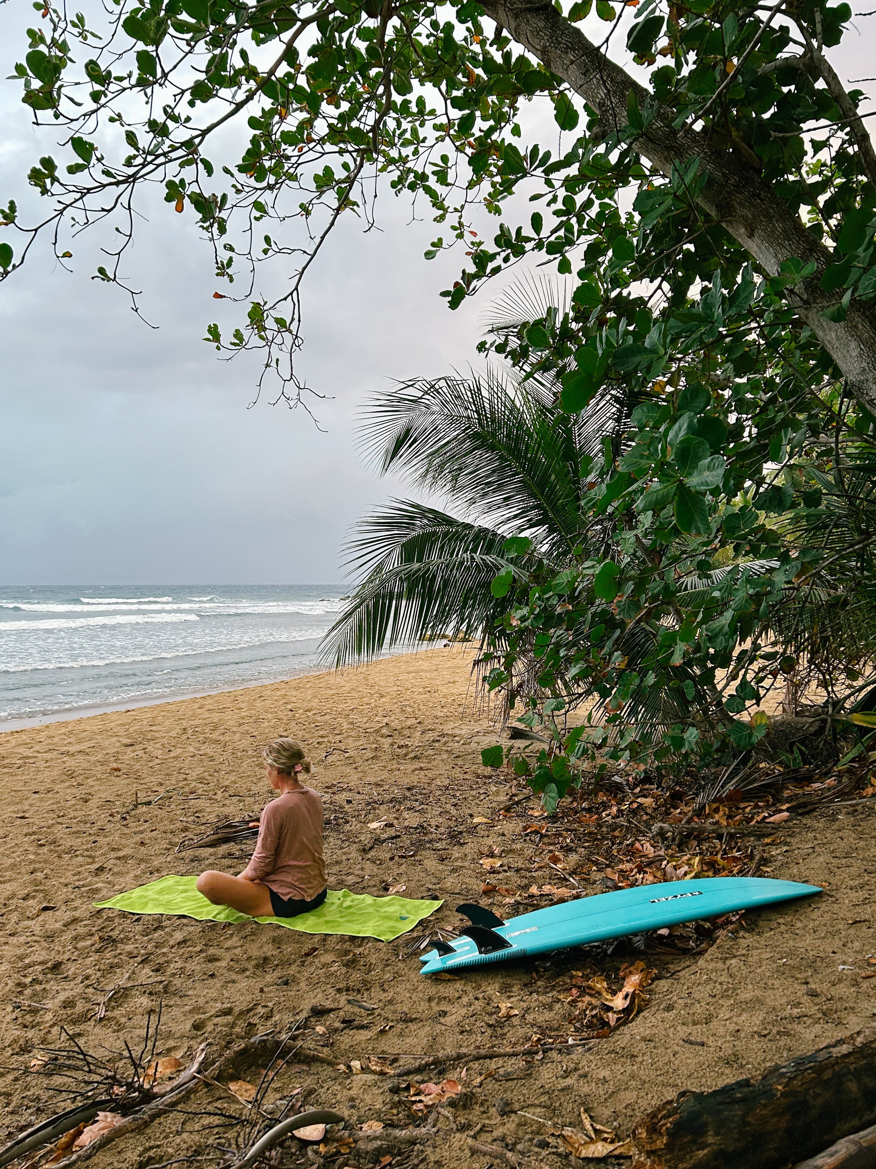 Cait na praia, sentada num Yogitoes toalha ao lado da sua prancha de surf azul