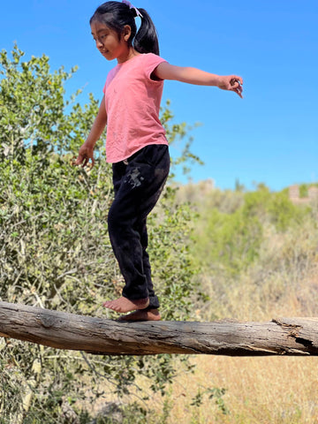 Kleines Mädchen hält das Gleichgewicht beim Laufen auf einem Ast