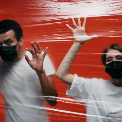 Man and woman wearing face masks behind plastic wrap