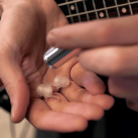 Hands holding EarPeace MUSIC PRO ear plugs and guitar