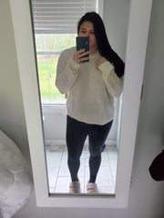 woman standing in front of mirror taking selfie in cream chic sweater and black leggings