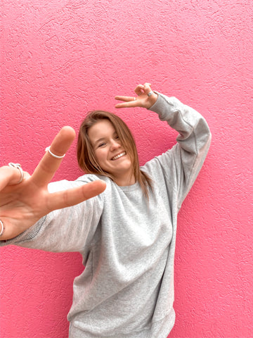 girl in front of pink wall holding peace sign