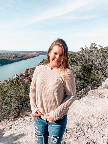 girl standing on overlook in pink sweater and distressed jeans