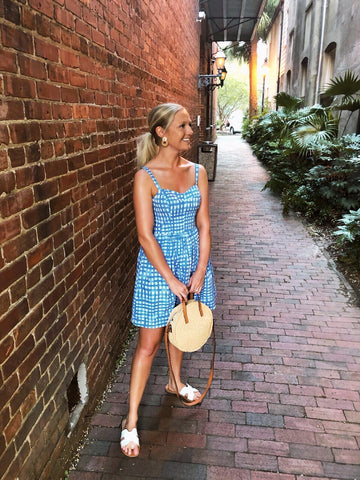 woman in plaid dress with boho bag in front of brick wall