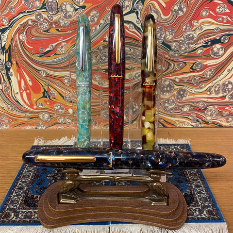 Red, tortoise shell, seaglass, and blue Esterbrook fountain pens on a marbled background with Persian Rug coasters underneath.