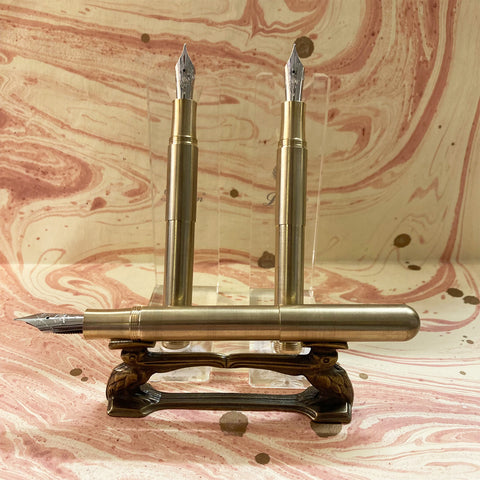 Two Kaweco Supras with extenders, with a Kaweco Supra without extender in the foreground on a pen stand, all on marbled paper