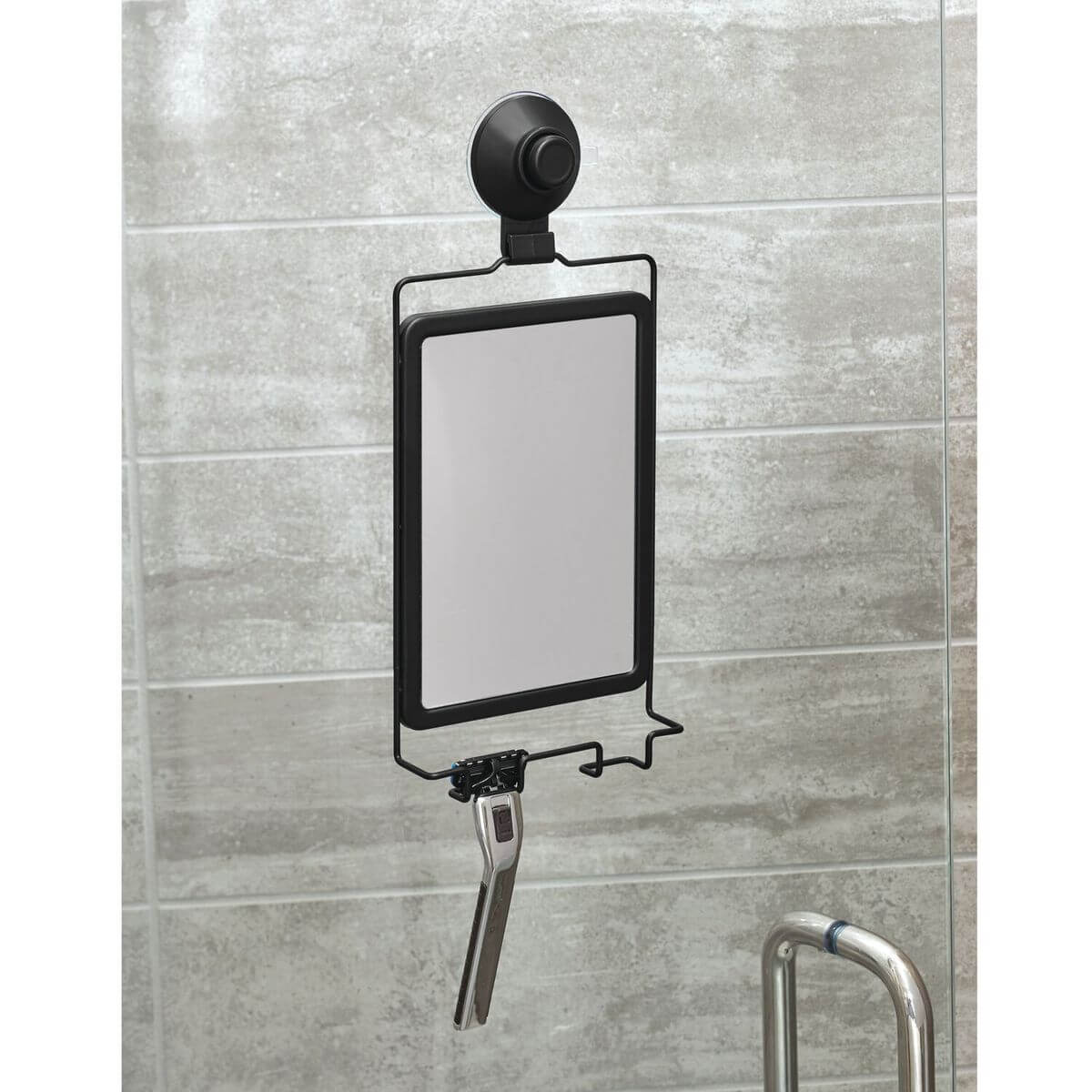 A matte black suction shaving mirror hung on tiles in the shower. There is a razor on the hanging hook.