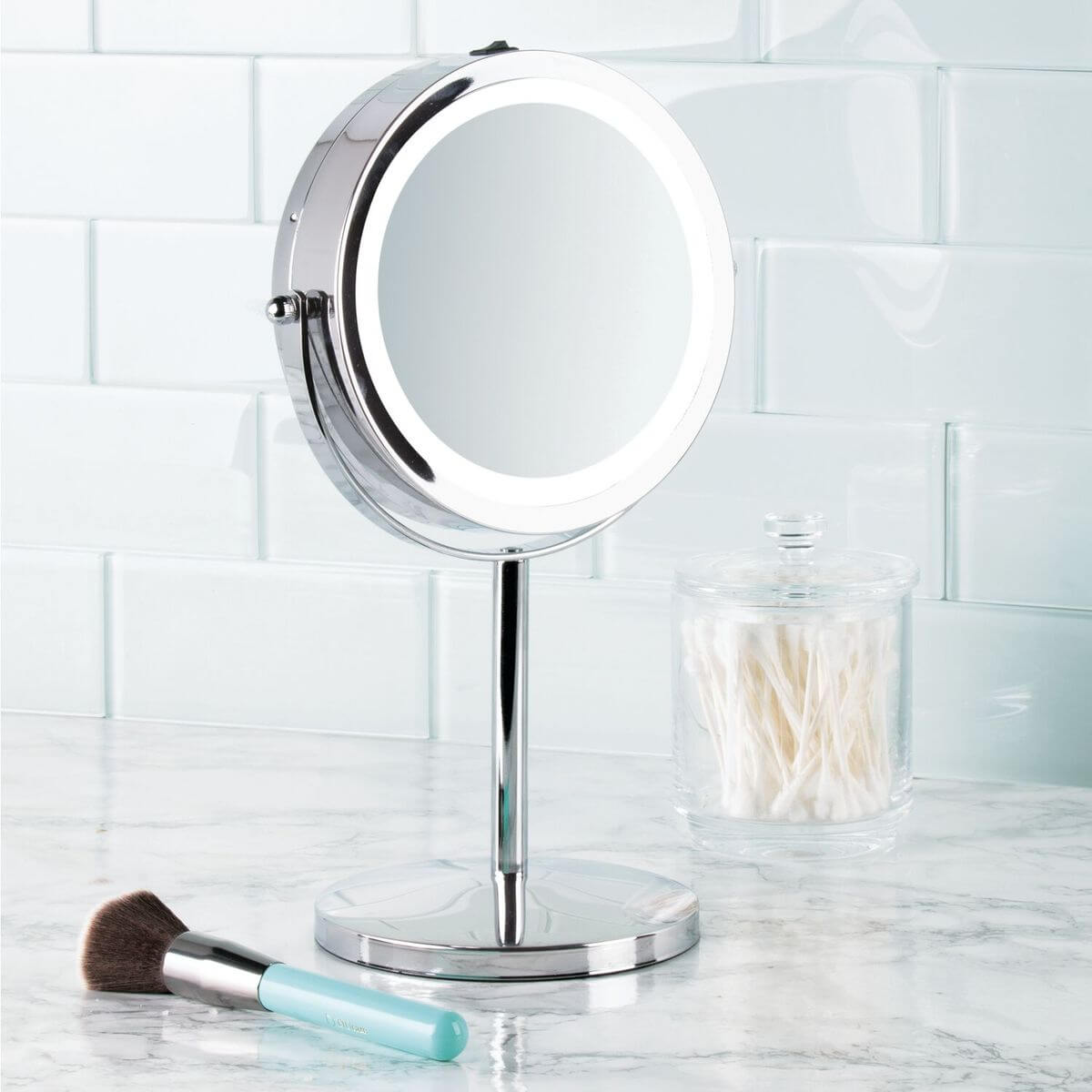A stainless steel makeup mirror with LED light standing on a marble top bathroom vanity