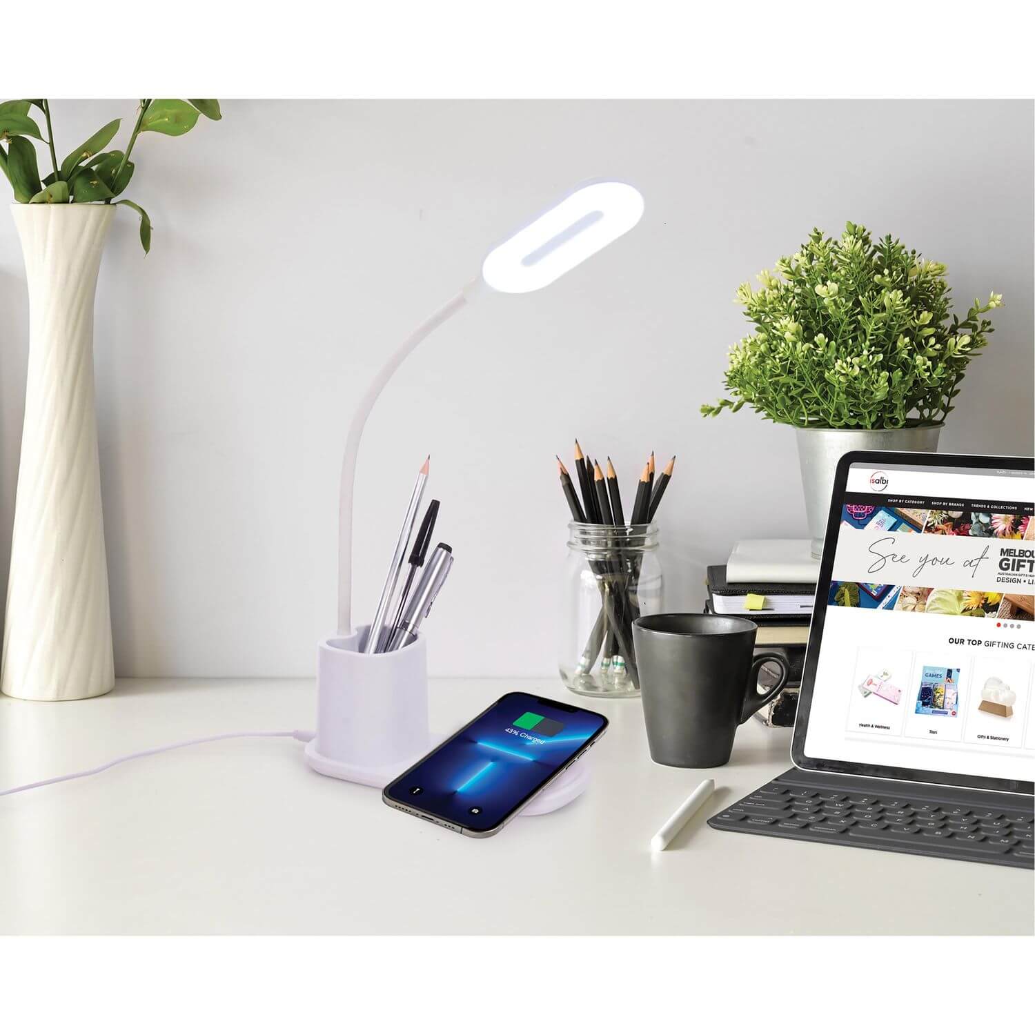 Light Up Desk Lamp sitting on a desk next to a tablet computer. There is a phone being wirelessly charged on the stand.