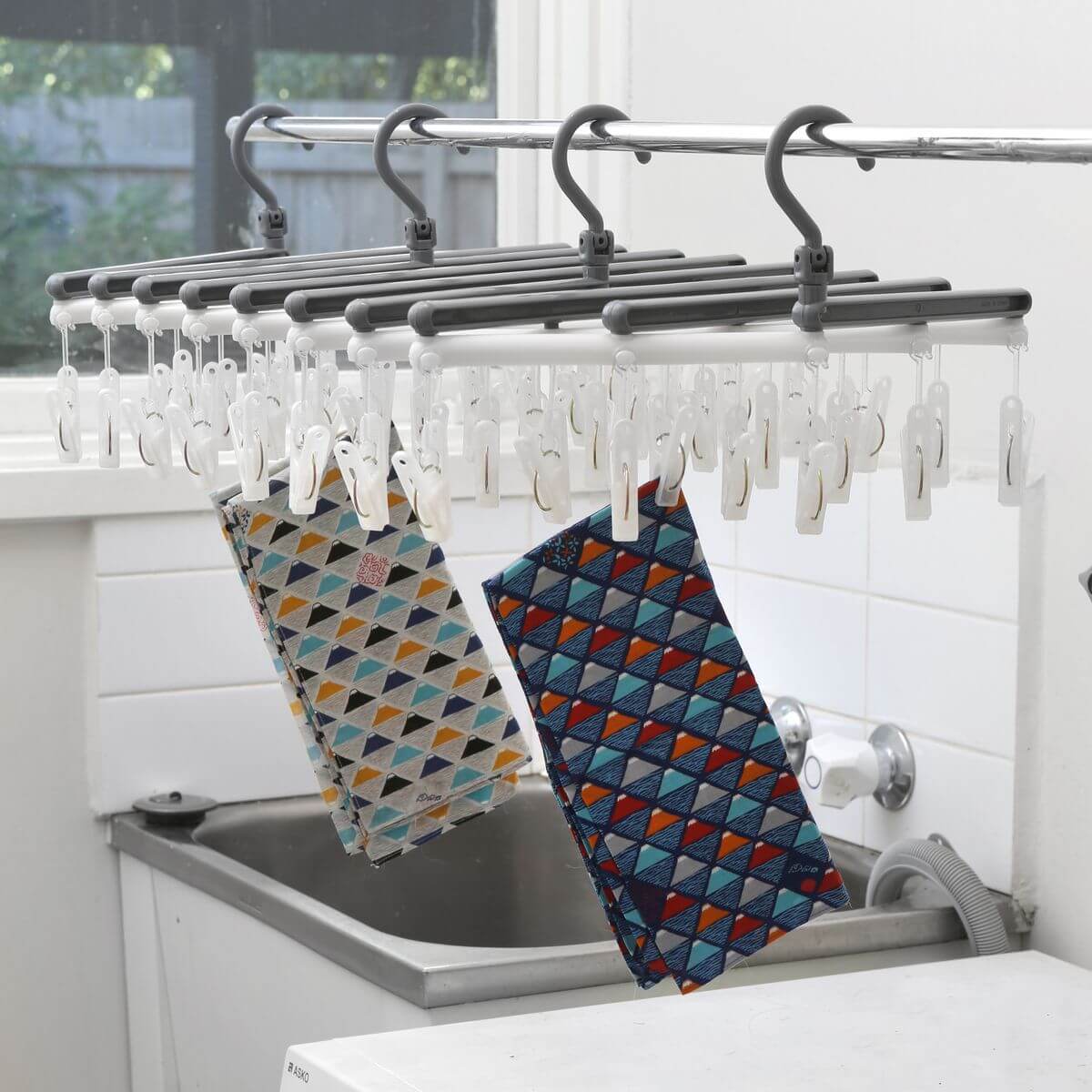 A white and grey mini peg clothes dryer hanging on a rail with small items drying on it