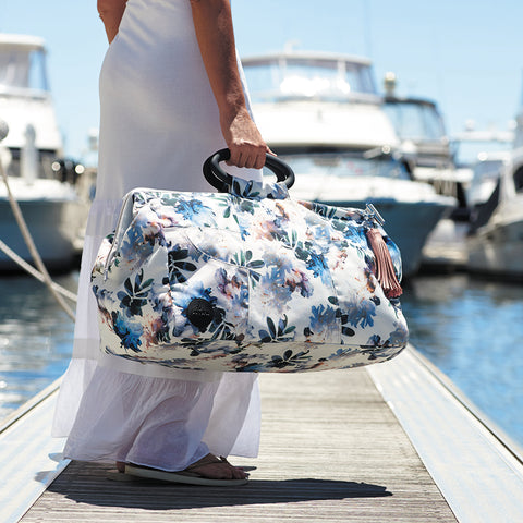 Floral travel bag in the hand of a woman walking on a jetty