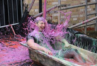 Man sat in a bathtub with purple slime being thrown over him to raise money for charity