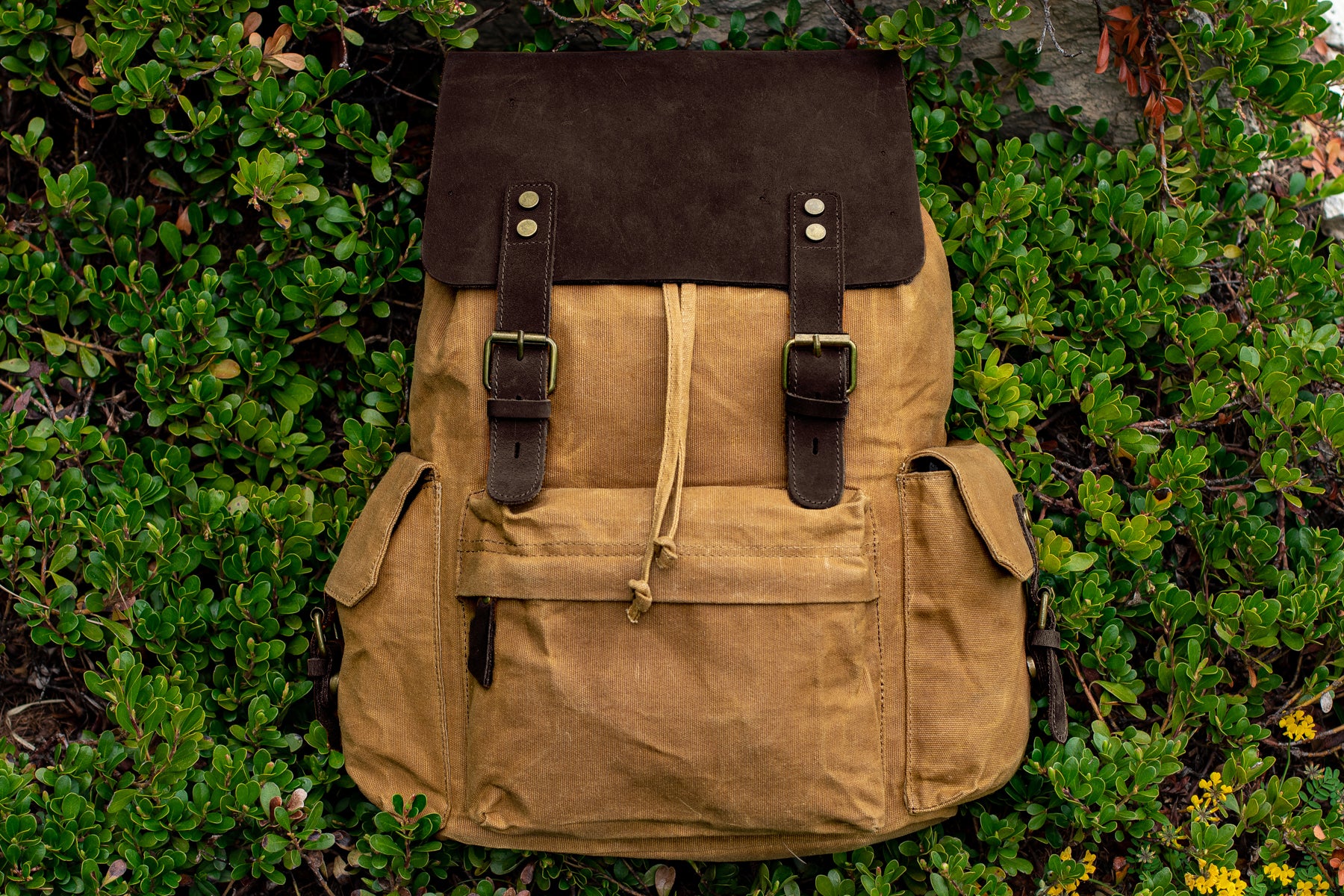 quality leather and waxed canvas backpack in khaki colors sitting on a field of wild grass outdoor