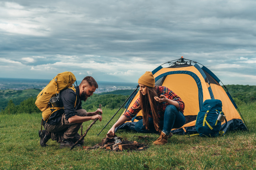 Couple de campeurs allumant un feu pendant qu'ils montent la tente du camp.