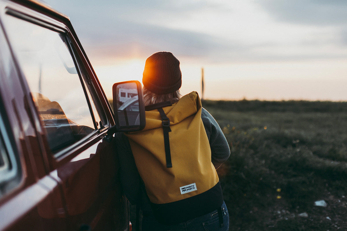 femme reposant sur un van au coucher du soleil et portant un sac à dos écologique en polyester recyclé de couleur jaune