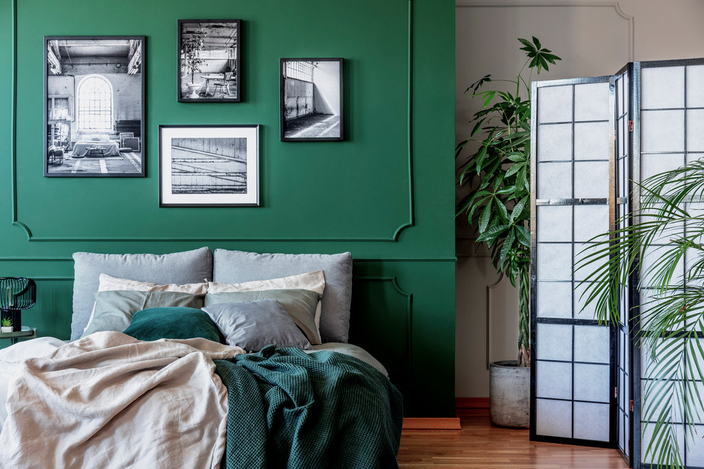 Gallery of black and white posters and photos on emerald green wall in trendy bedroom