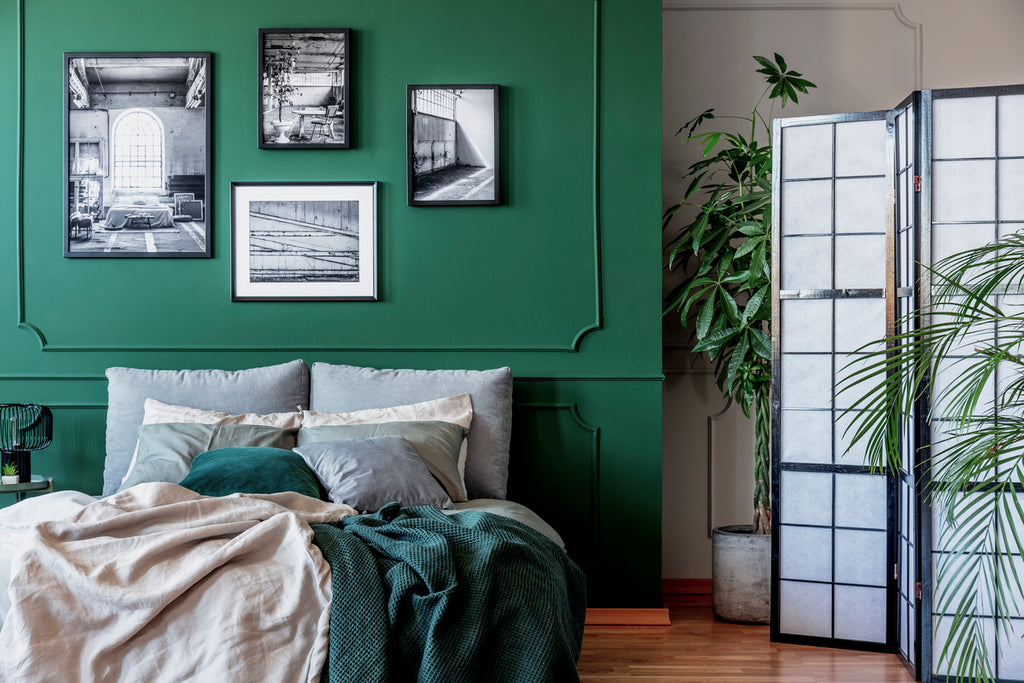 Galerie d'affiches et de photos en noir et blanc sur un mur vert émeraude dans une chambre à coucher branchée