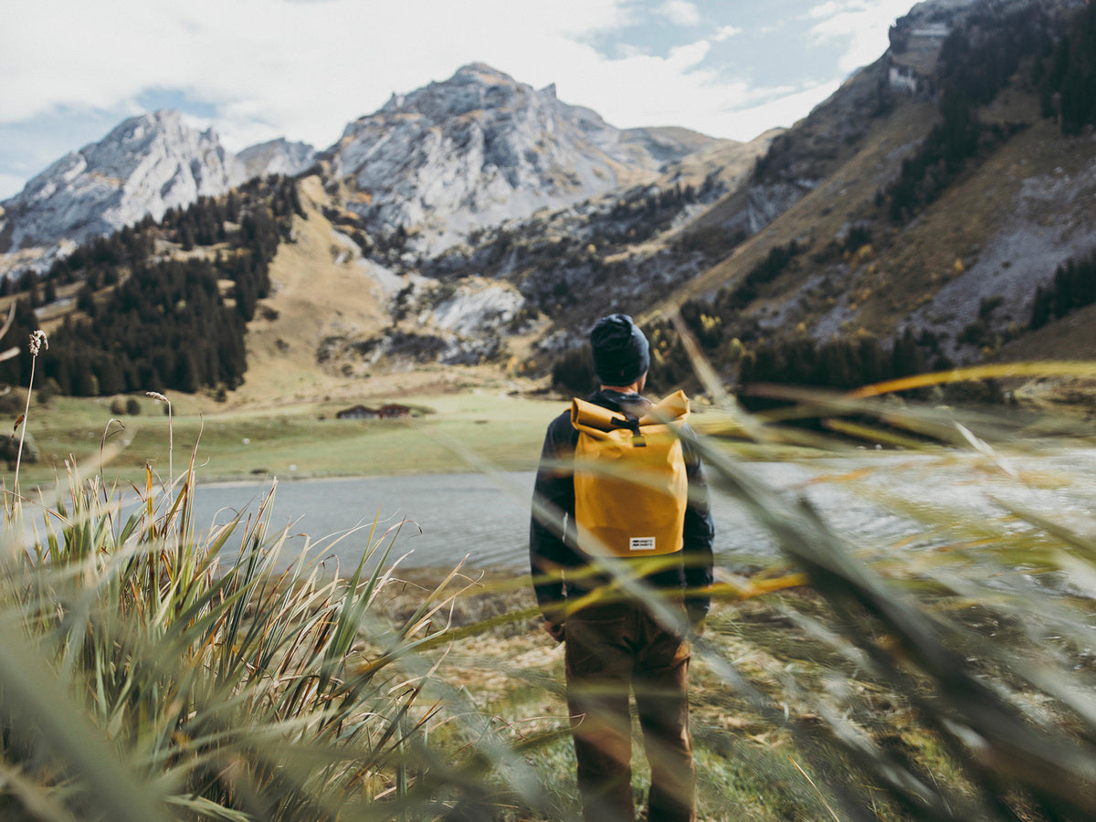 hiker in the mountain looking at a lake wearing a yellow eco-friendly bag