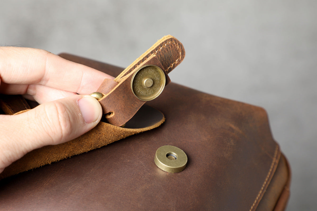 close up view of a magnetic buckle on a leather travel duffle bag