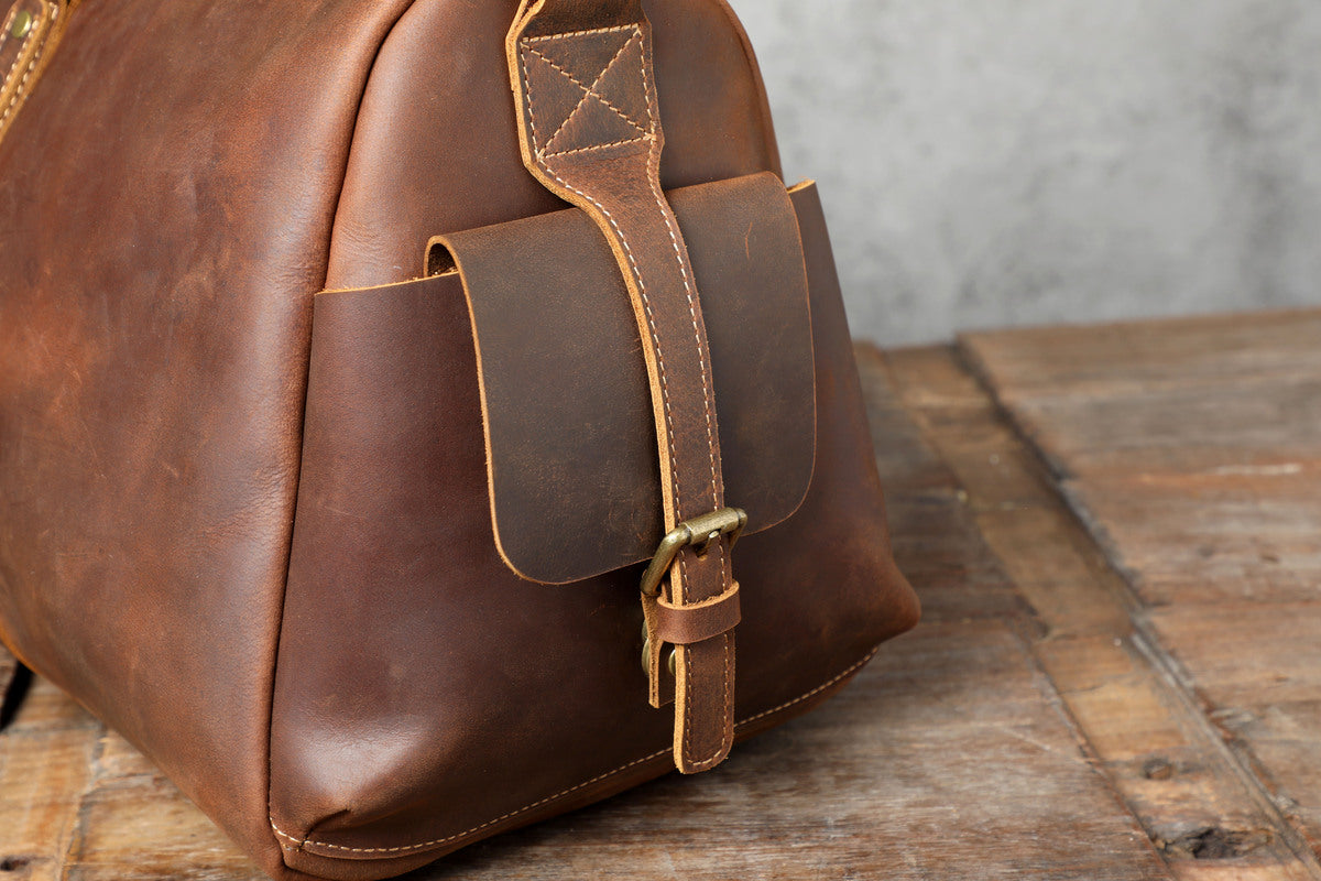 side flap pockets with magnetic buckles of a leather duffle bag