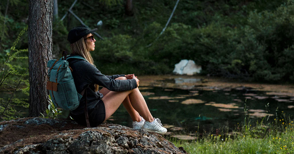 women sitting on a rock near a mountain lake wearing a vintage light blue canvas and leather backpack with padded shoulder straps