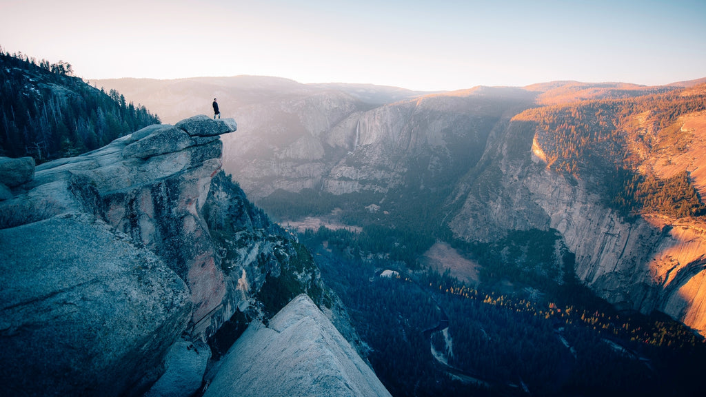 man standing at the edge of a rock at the Glacier Point at the Yosemite National Park at the sunset