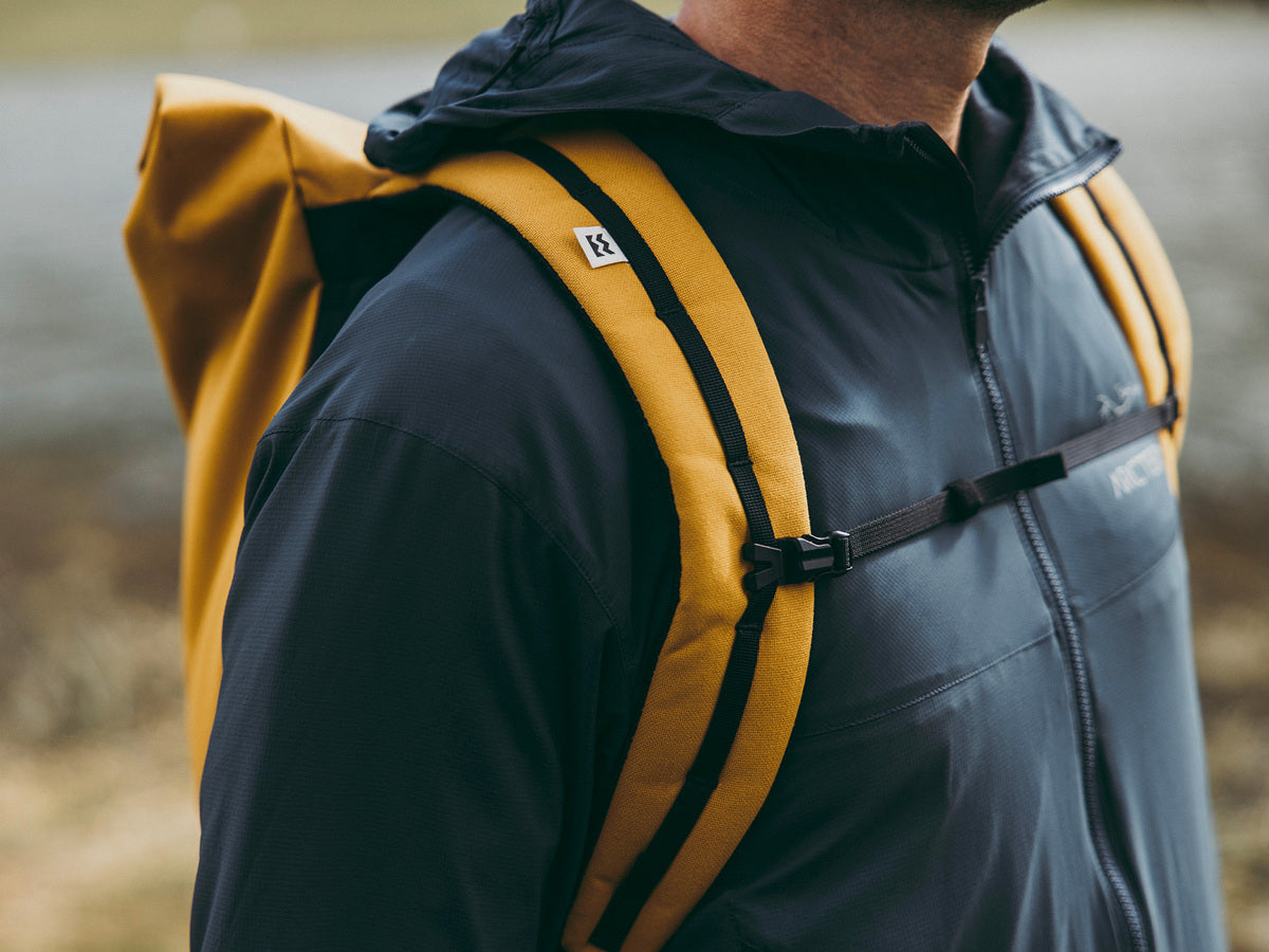 lifestyle close up view of the mesh adjustable padded shoulder straps and sternum belt of a yellow roll top eco rucksack from the brand mero mero