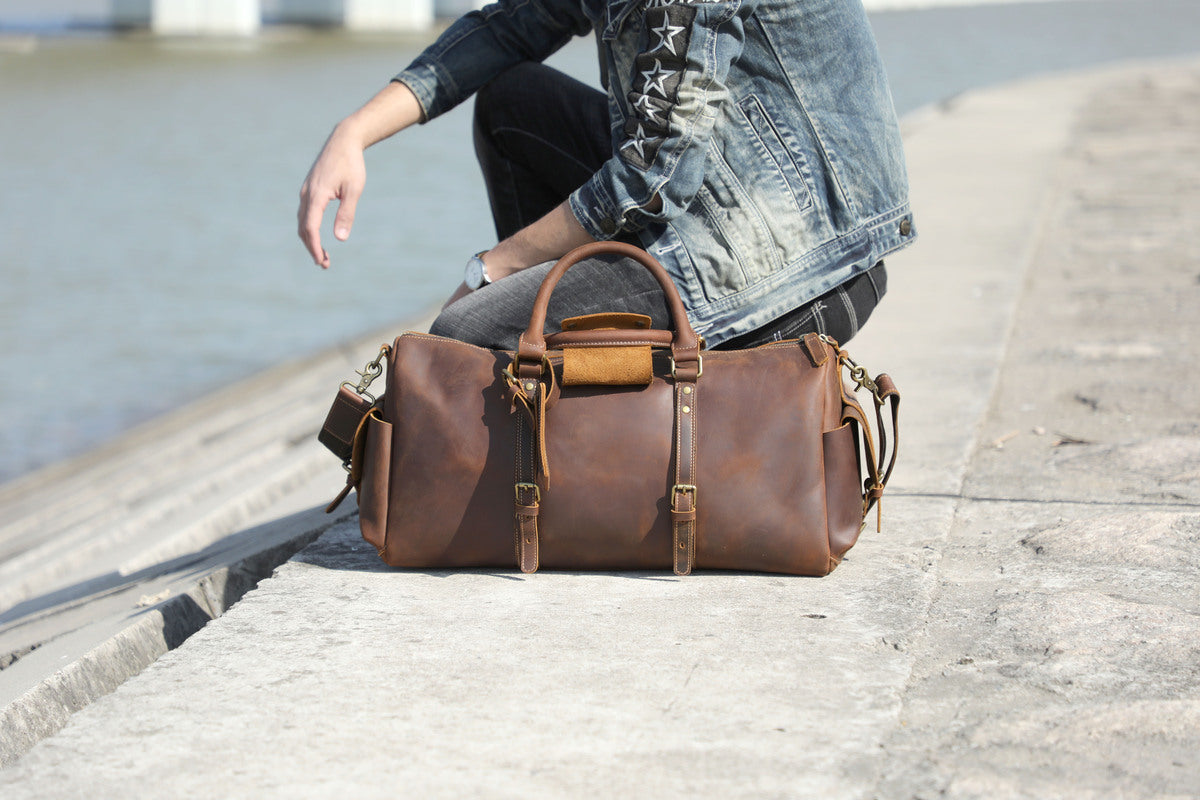 man sat on a river banks with a leather duffle bag at his side