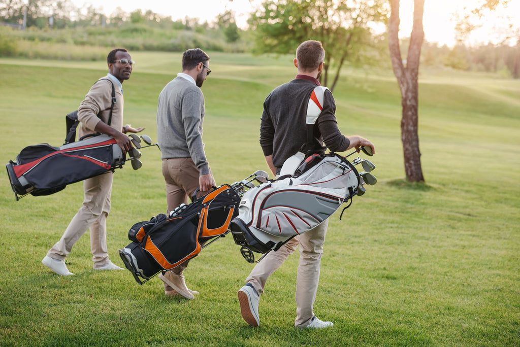 Joueurs de golf multiculturels avec des sacs de clubs de golf marchant sur le parcours de golf