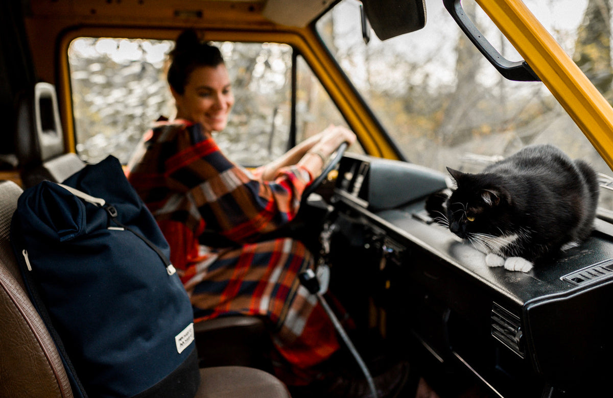 inside view of a van with a women and a vegetable tanned leather and navy blue recycled polyester rooll top backpack