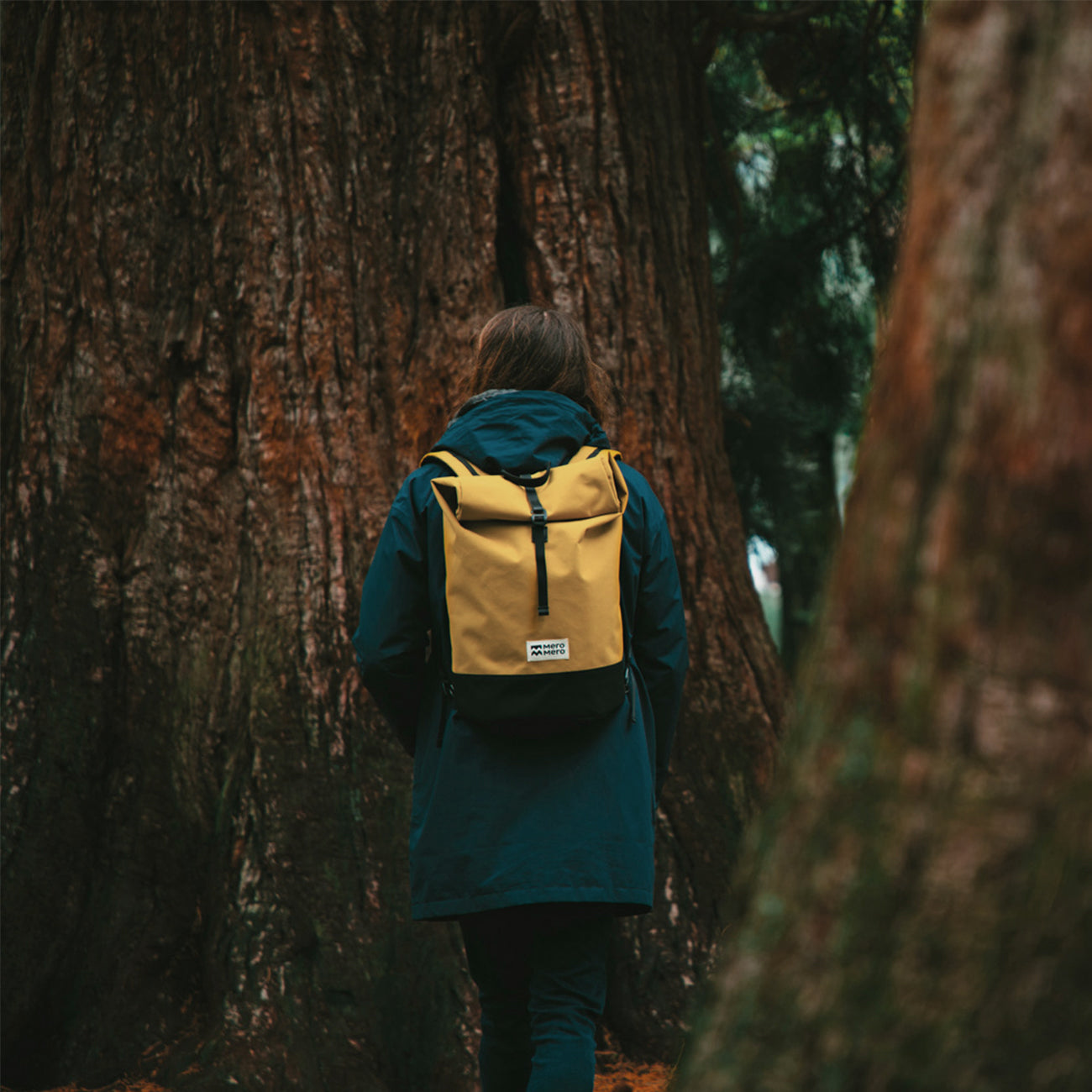 femme marchant dans une forêt avec un sac à dos Coursier de voyage roll top en bouteilles recyclées jaune mero mero