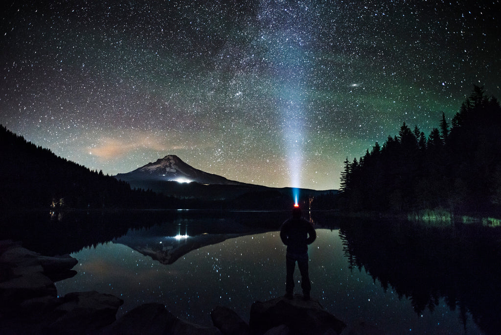 Silhouette d'un homme portant une lampe frontale, debout au bord d'un lac, avec un ciel étoilé.