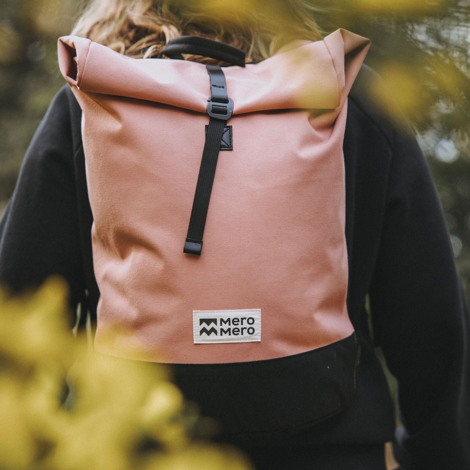 woman hiking wearing a pink eco friendly roll top backpack from mero mero