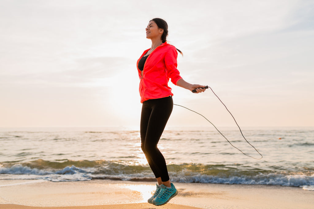 Jeune femme séduisante en tenue de sport faisant des exercices sportifs au lever du soleil sur une plage.