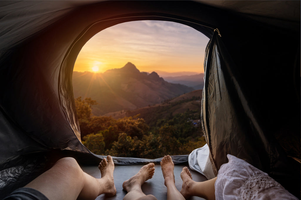 Jeune couple allongé dans une tente de camping et regardant le coucher de soleil sur la montagne