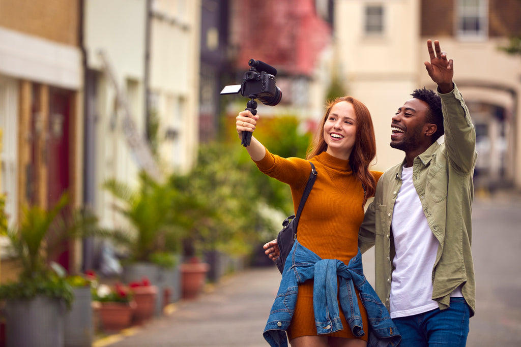 Jeune couple traversant la ville ensemble en train de faire un Vlogging avec une caméra vidéo sur un trépied à main