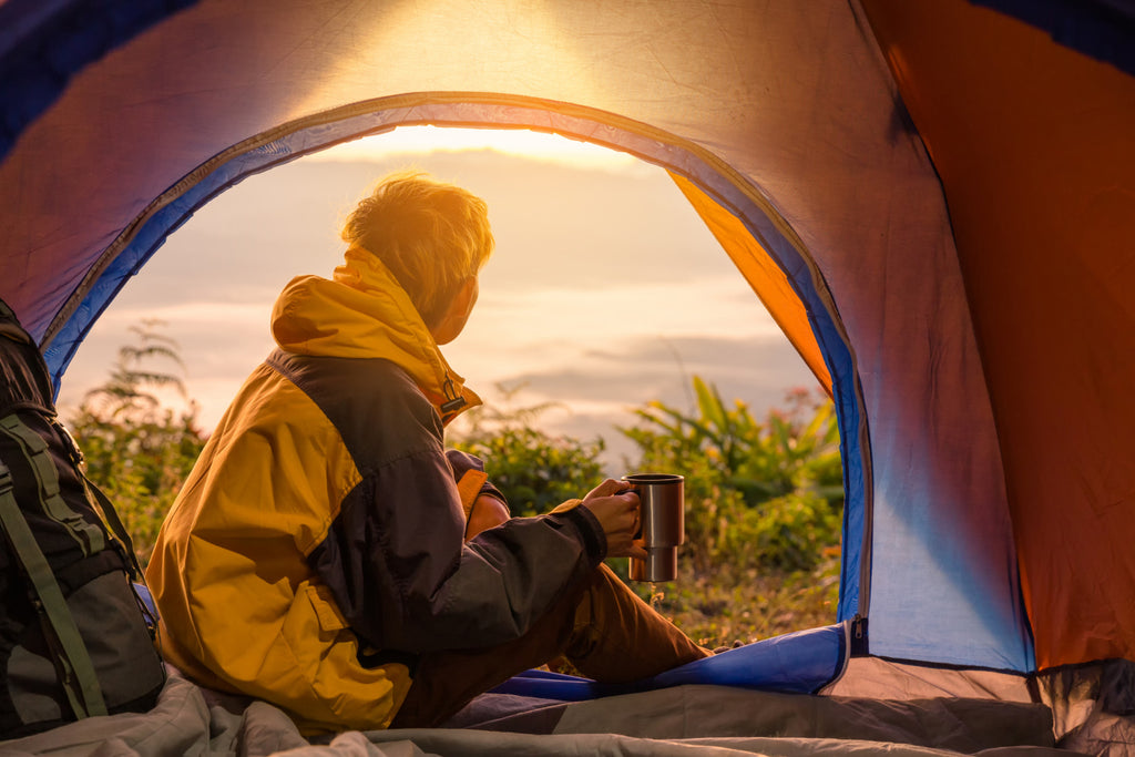 Un jeune homme assis dans la tente, tenant une tasse de café.