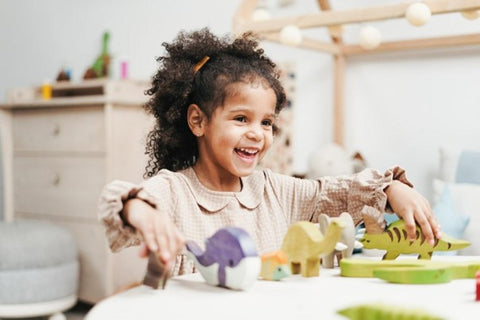 Laughing young girl playing with wooden toys on a white table.