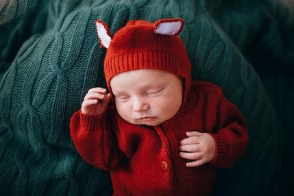 A newborn baby in knitted red woolen jumpers sleeping.