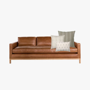A leather sofa mockup with Darcy, Karina, and Dara lumbar pillow covers from Colin and Finn.